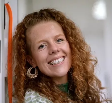 Kirsty Taylor is a white woman with long curly ginger hair.