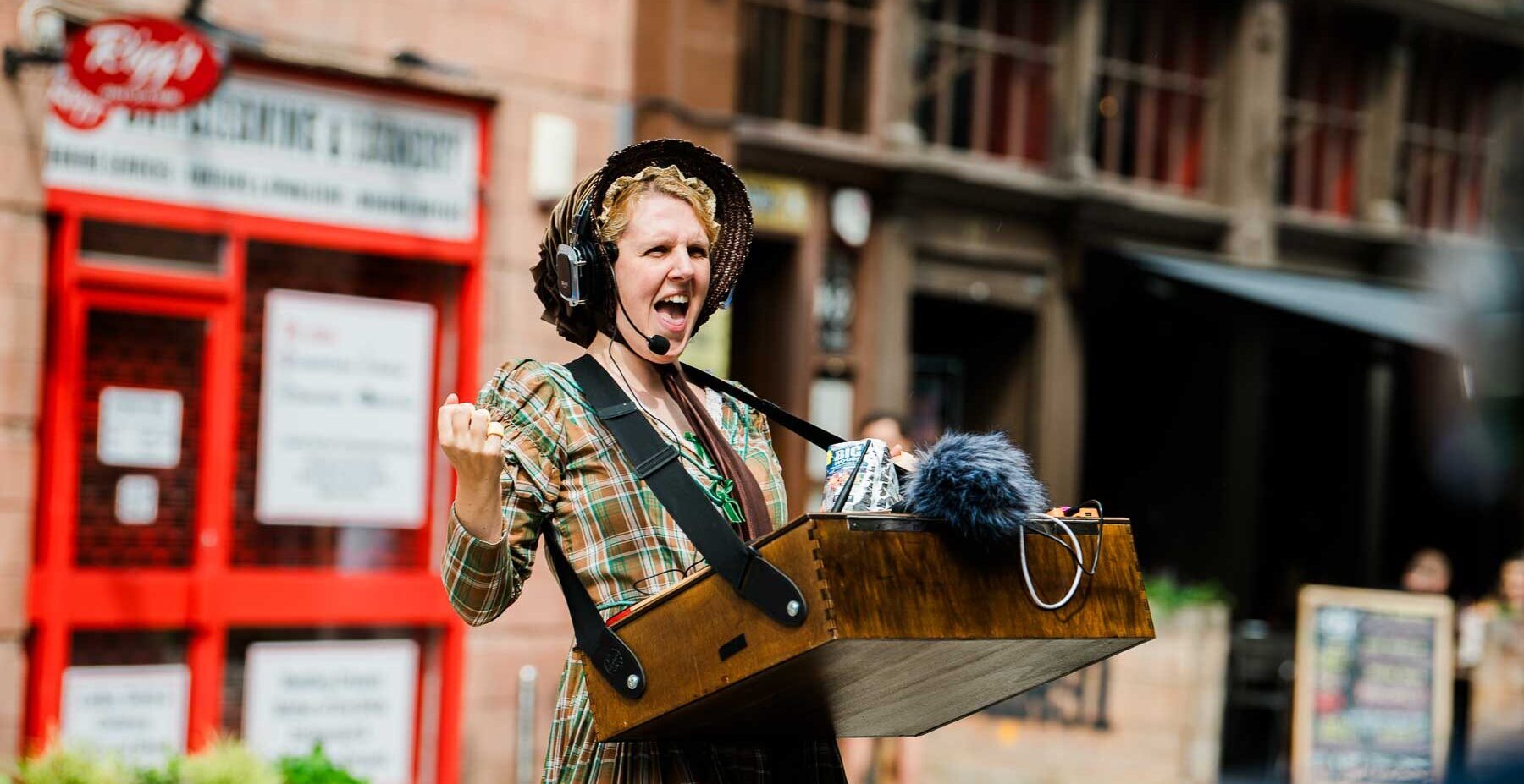 Fran Bundey dressed as Charlotte Bronte and wearing silent disco headphones and speaking to a street audience out of shot