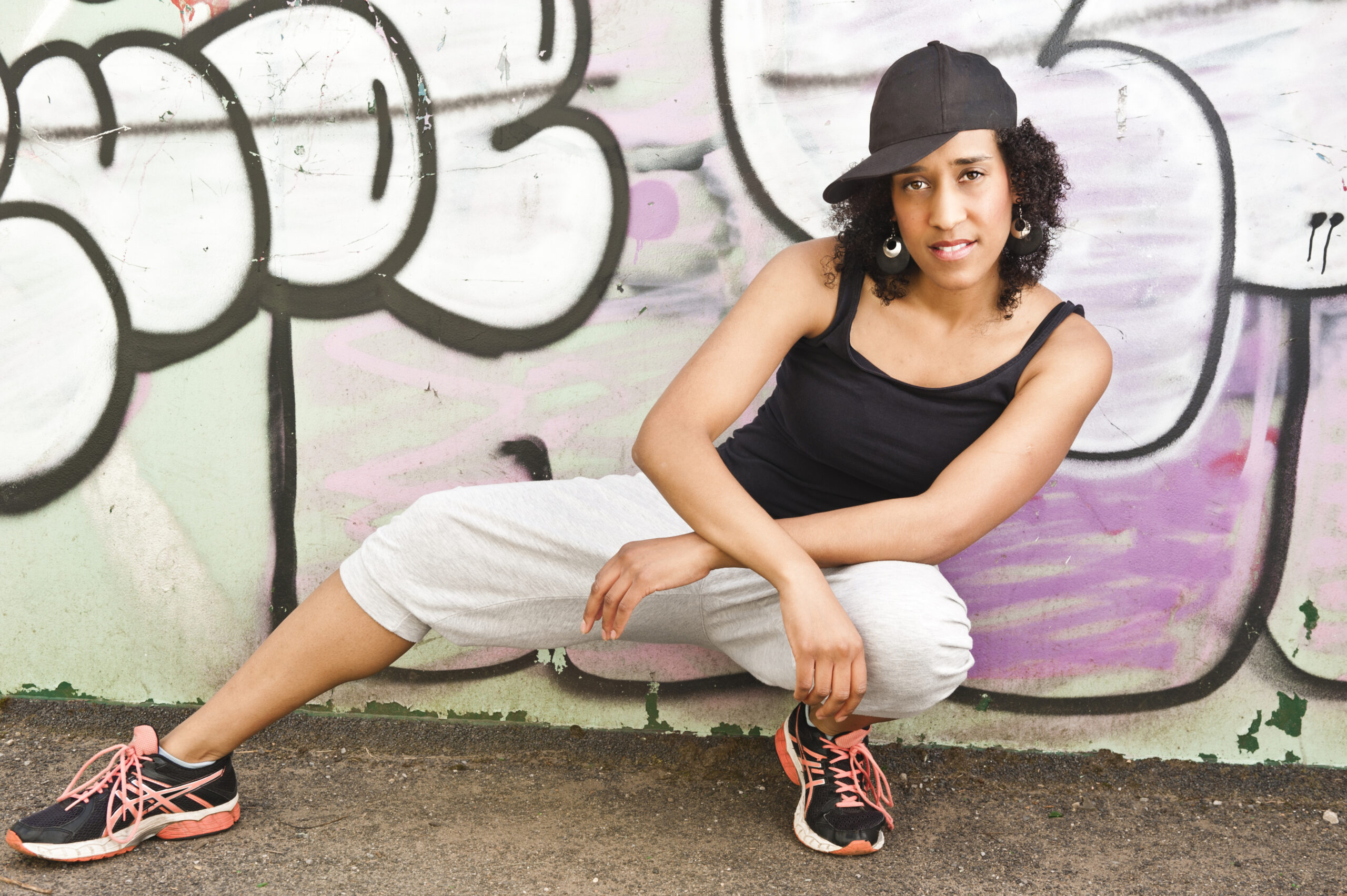 Tricia in a side lunge pose in front of a wall graffitied in pink and white text