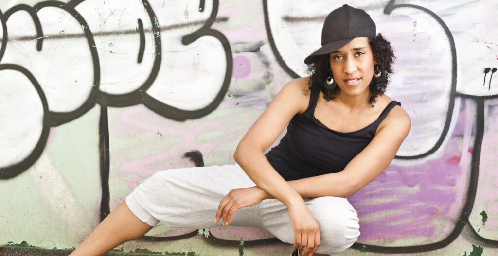 Tricia in a side lunge pose in front of a wall graffitied in pink and white text