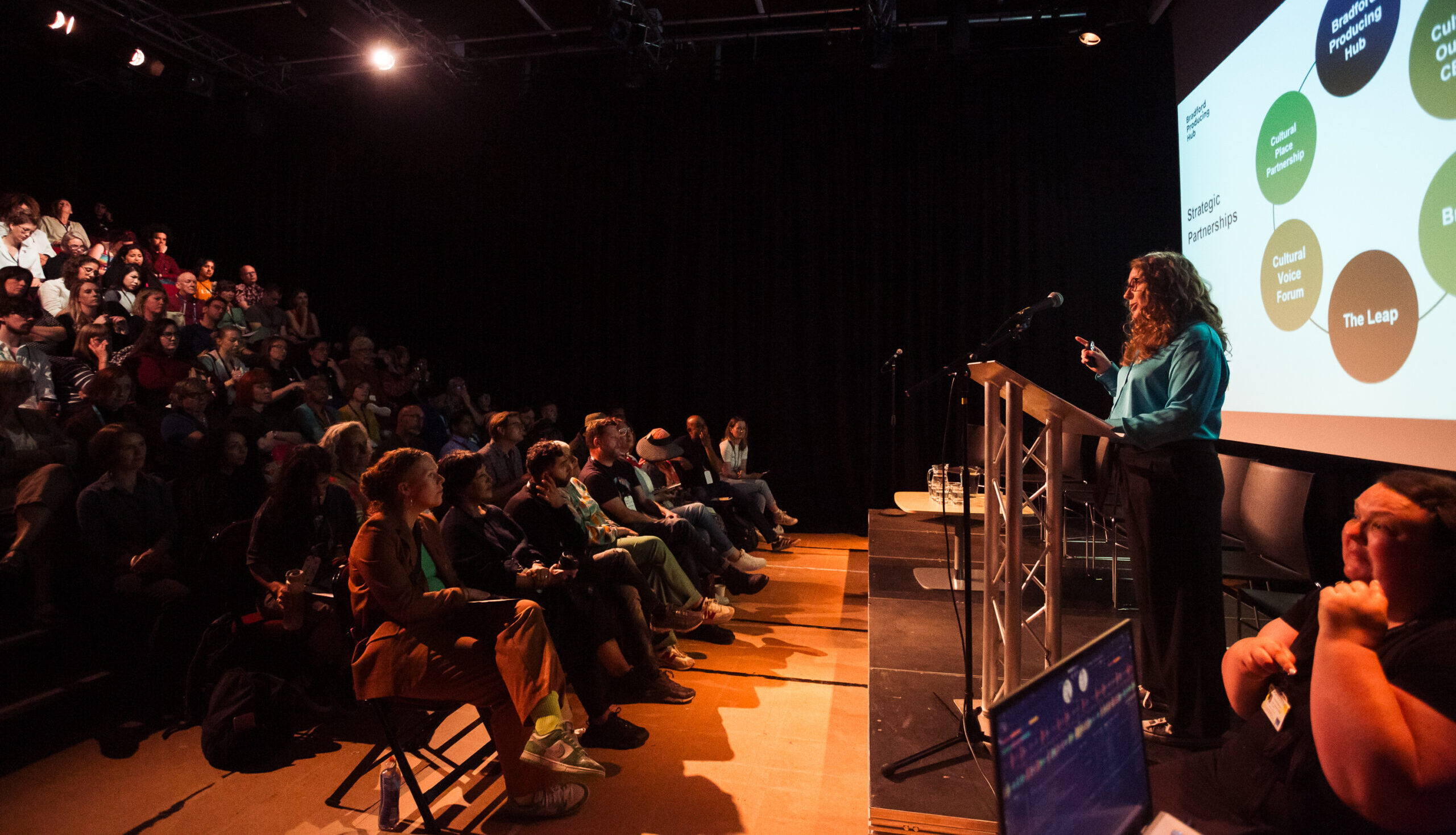 Exec. Director of Bradford Producing Hub speaking at a lectern to conference delegates