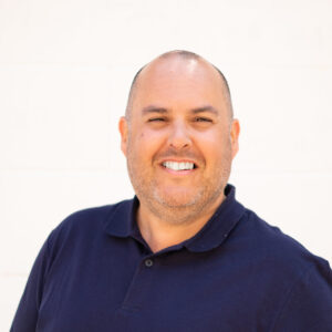 Headshot of Dean Shaw, a white man in his forties. He has very short dark hair, brown eyes and wears a navy polo t-shirt.