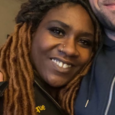 Close up photo of Monique Slattery, a black woman with long dreadlocks half tied up and a nose ring.